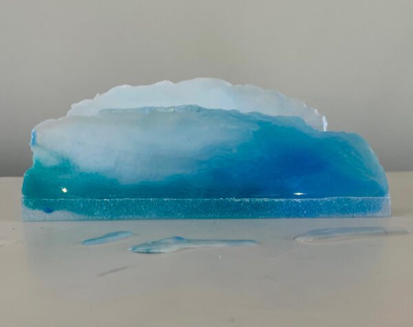 A resin art piece resembling a cross-section of the ocean, with varying shades of blue, displayed on a white surface.